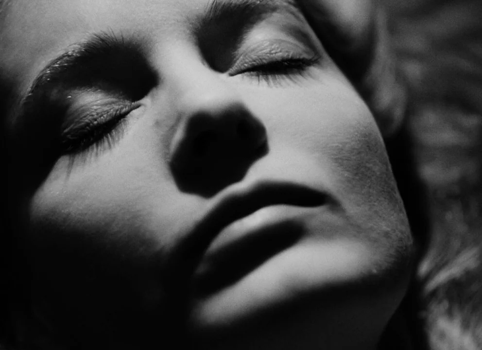 Othello (1952) movie still: closeup — The frame shows a close-up of a woman's face in low lighting. She lies still with her eyes closed in a dark…