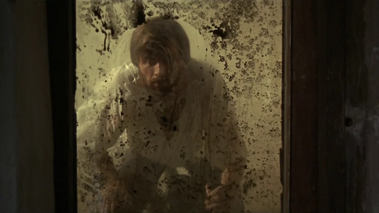 A Quiet Place In The Country (1968) movie still: medium — A man is positioned behind a severely tarnished, grime-streaked glass pane in a dim space.…