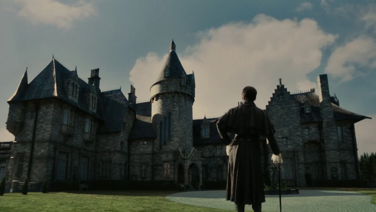 Dark Shadows (2012) movie still: wide — A large multi-story stone manor with a prominent central turret stands on a lawn. A man in a dark coat…