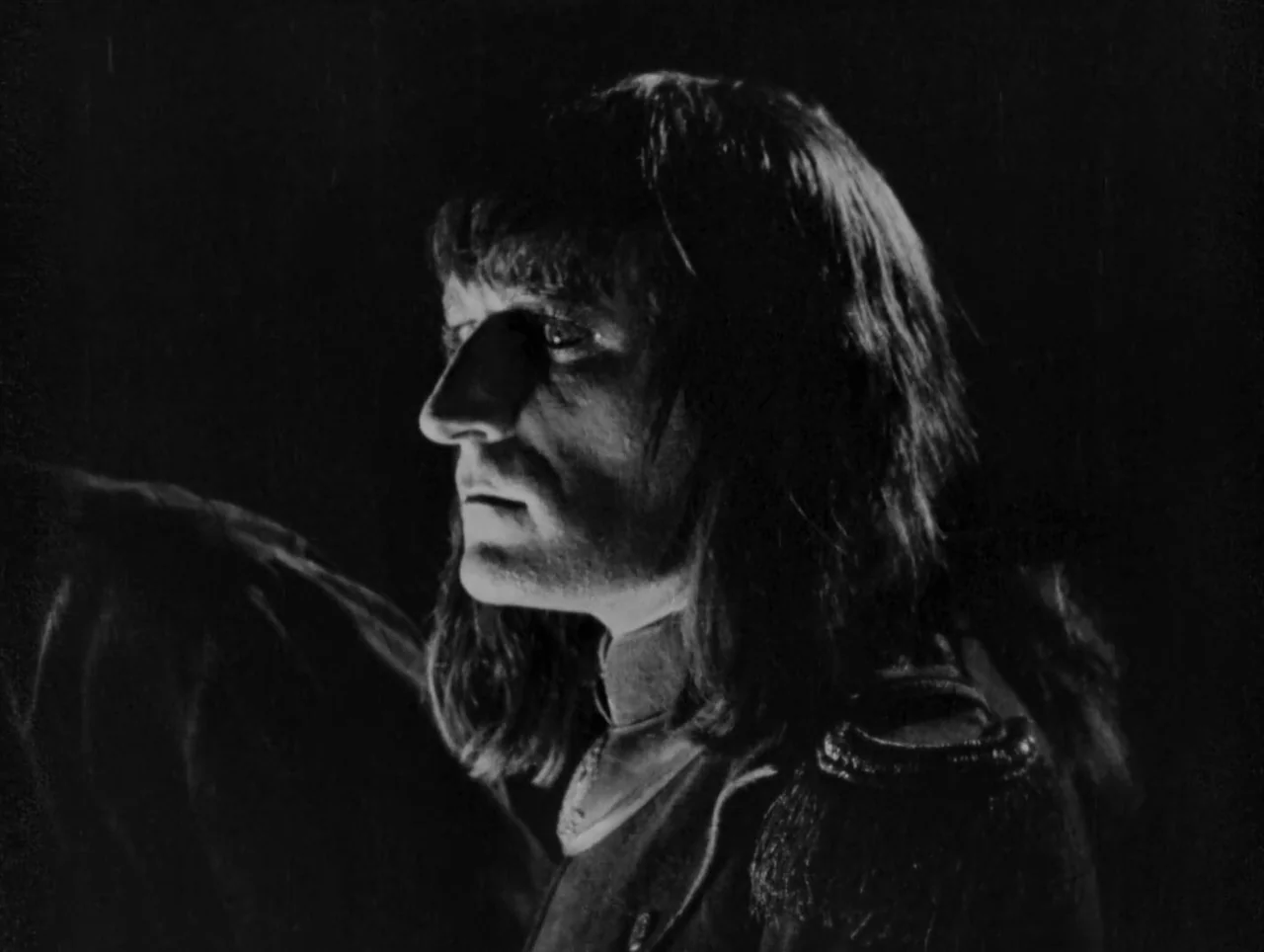 Napoleon (1927) movie still: closeup — A dark, underexposed environment isolates a person in a military uniform against black. The character remains…