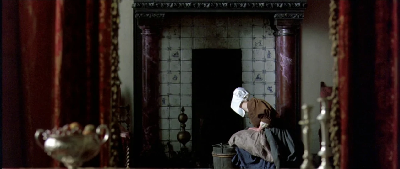 Girl with a Pearl Earring (2003) movie still: medium — A stone hearth with tiled back wall frames a woman in period clothing. She kneels on the…