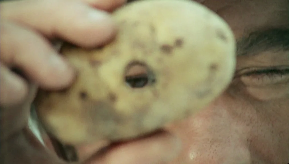 The Great Silence (1968) movie still: closeup — An indoor space serves as the background for a man's face and hand. A human hand holds a raw potato…