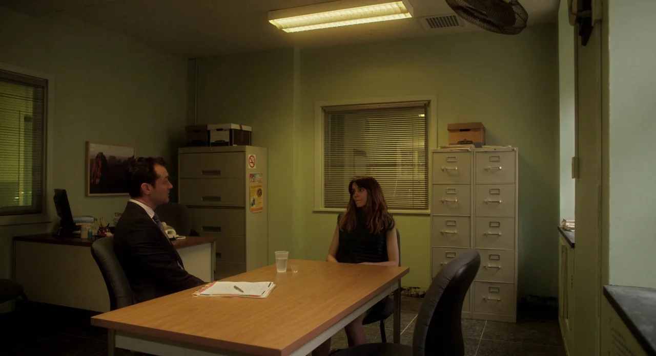 Side Effects (2013) movie still: medium — A spare, green-walled room contains two metal filing cabinets and a central wooden table. A man in a suit…