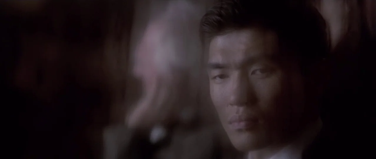 Snow Falling on Cedars (1999) movie still: closeup — A man stands in a dark, indistinct interior setting with shadows obscuring the surroundings. He…