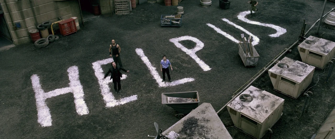 Resident Evil: Afterlife (2010) movie still: wide — A paved industrial lot features large painted white letters spelling out the word HELPUS. Three…