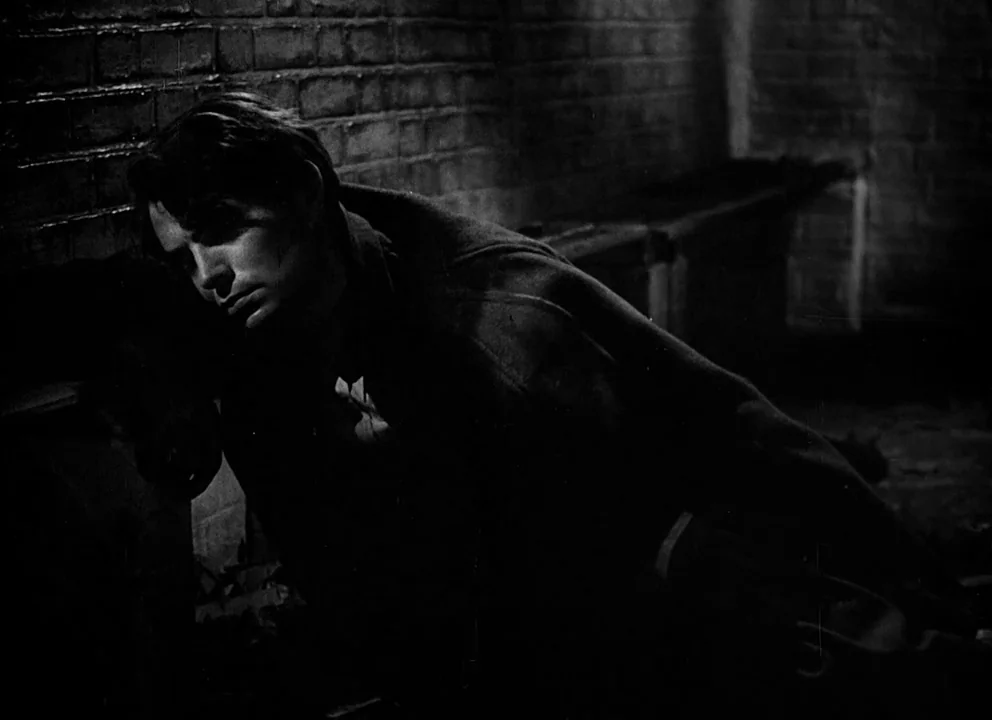 Odd Man Out (1947) movie still: medium — A dark, textured brick wall in an urban outdoor setting at night. A man rests his head against the masonry…