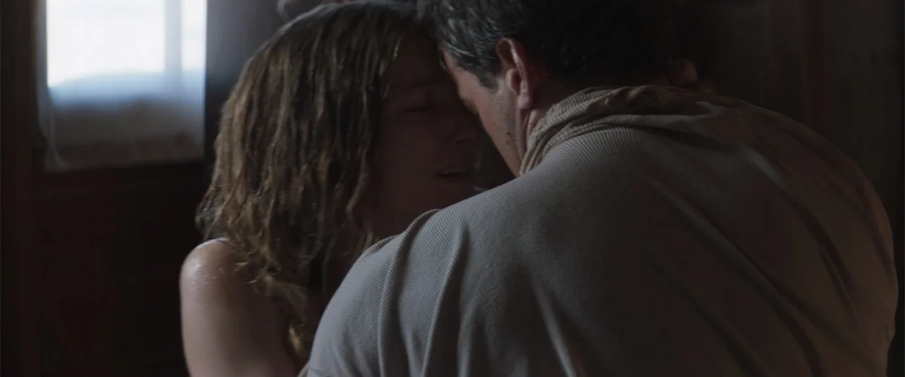 The Wind (2005) movie still: closeup — A dimly lit room with a single window provides light for a close interaction. A man and woman hold each other…