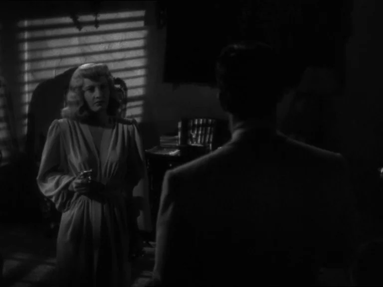 Double Indemnity (1944) movie still: medium — A dimly lit room with venetian blinds casting shadows on the wall. A woman in a robe stands facing a…