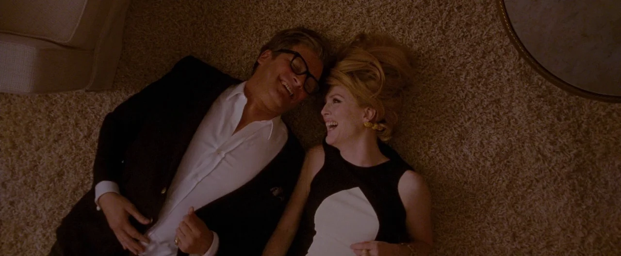 A Single Man (2009) movie still: medium — A man and a woman lie on a plush tan carpet in a room. They face each other and laugh while lying on the…