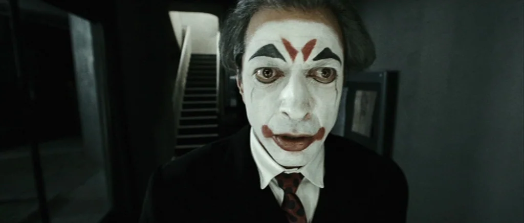 Adam Resurrected (2008) movie still: closeup — A dimly lit indoor corridor features a staircase visible in the blurry background. A man wearing…