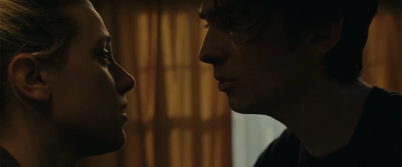 Chemical Hearts (2020) movie still: closeup — An interior space with a dimly lit window featuring hanging curtains. A young man and a woman stand…