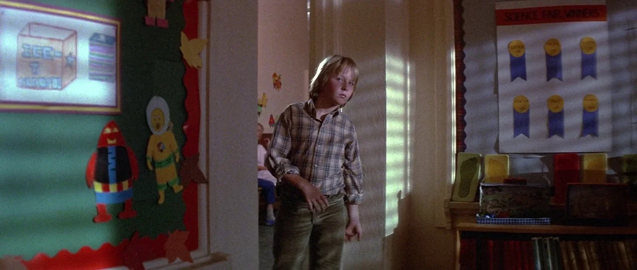 Invaders From Mars (1986) movie still: medium — A school hallway decorated with paper cutouts and a science fair awards poster. A young blond boy…