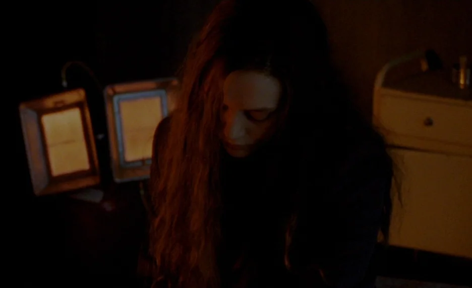Pola X (1999) movie still: medium — A dimly lit interior space contains a wooden bedside stand and two glowing lamps. A young woman with long hair…
