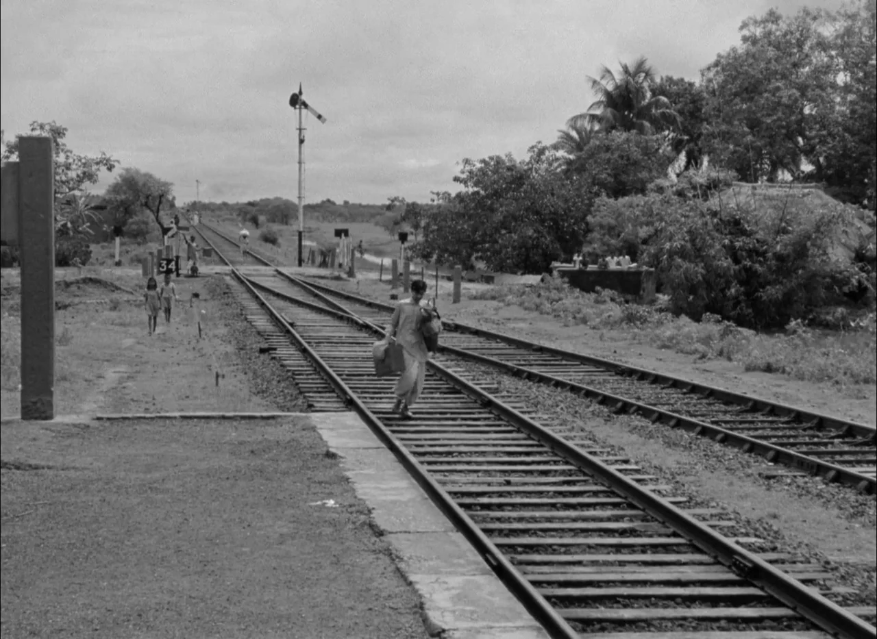 Aparajito (1956) movie still: wide — A rural railway line stretches into the distance under a clouded, overcast sky. A young boy walks along the…