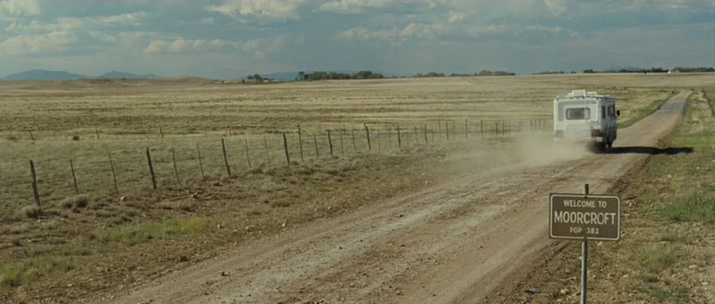 Paul (2011) movie still: wide — An arid, grassy expanse stretches under a bright sky with sparse white clouds. A white recreational vehicle drives…