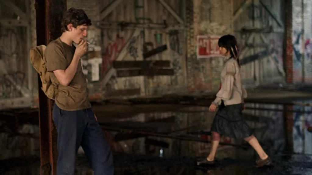 Undertow (2004) movie still: fullbody — A spacious, dilapidated industrial warehouse features graffiti-covered wooden walls and a flooded concrete…