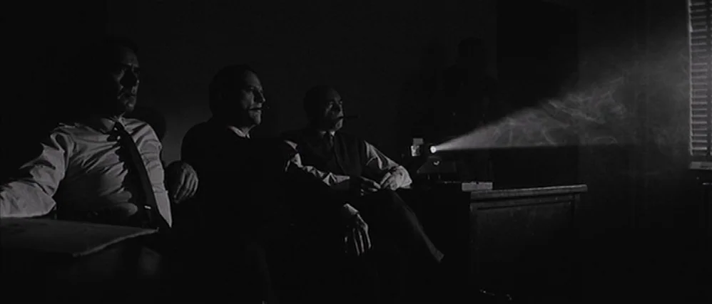 In Cold Blood (1967) movie still: medium — A dark, wood-paneled room containing three men seated in front of a projector. A visible beam of light…
