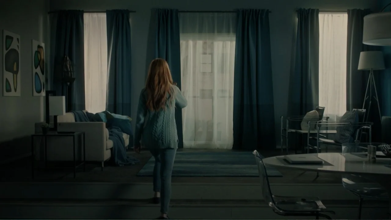 Sightless (2017) movie still: fullbody — A modern apartment living room features dark blue curtains and contemporary furniture on a dais. A lone…