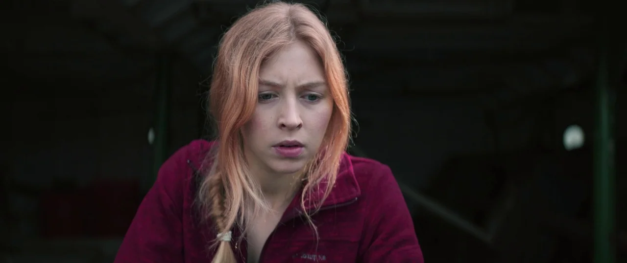 Sea Fever (2019) movie still: medium — A woman stands inside a dark enclosure with indistinct surroundings. She gazes downward with a focused…