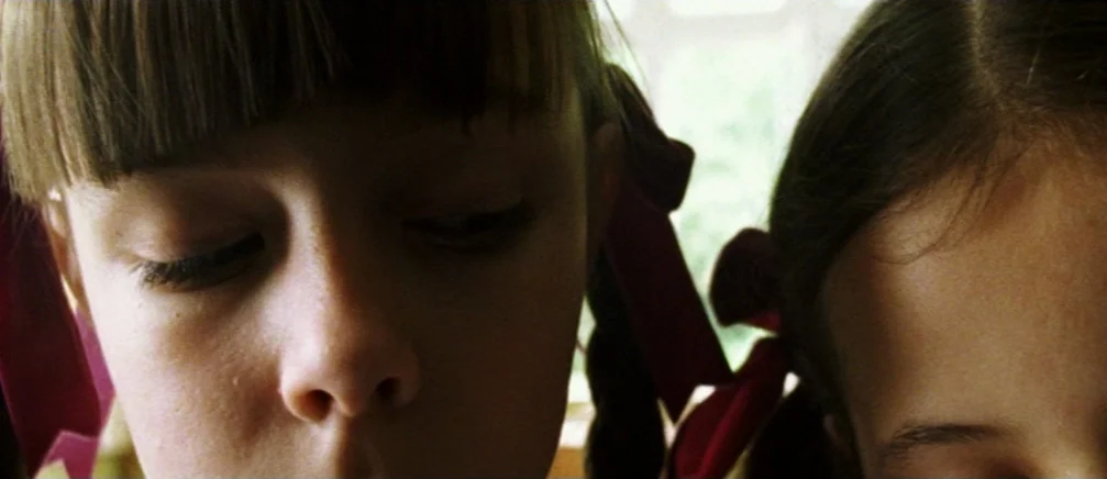 Innocence (2005) movie still: closeup — A close view shows two young girls with braided hair and red ribbons. They are looking down at a surface…