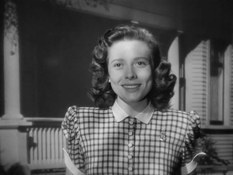 The Best Years of Our Lives (1946) movie still: medium — A woman stands on a house porch with wooden railings and columns behind her. She faces the…