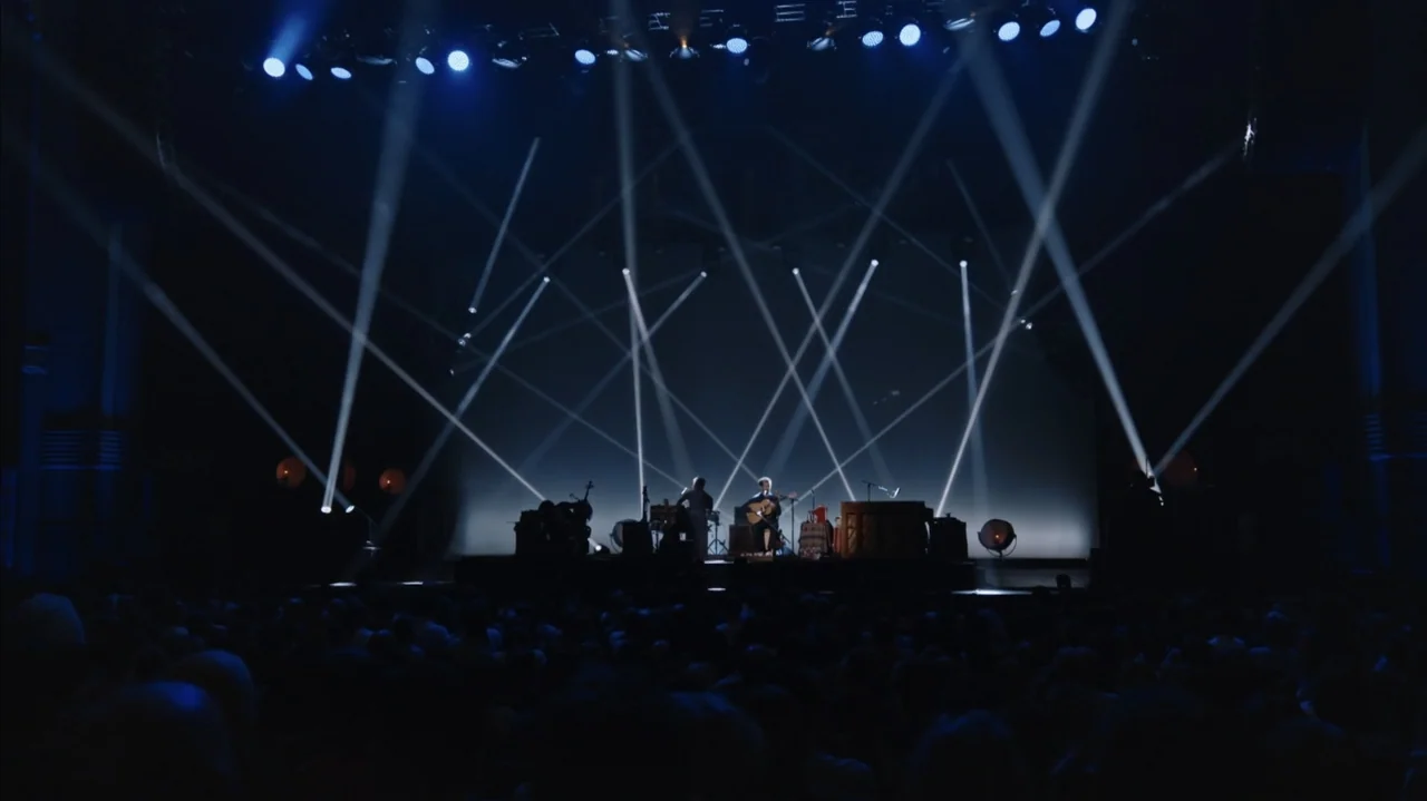 Flight of the Conchords: Live in London (2018) movie still: wide — A wide dark concert hall contains a small elevated platform holding several…