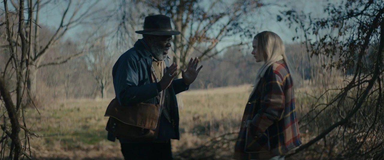 I'm Your Woman (2020) movie still: medium — A clearing at the edge of a woodland area features leafless trees and dry grass. An older man gestures…
