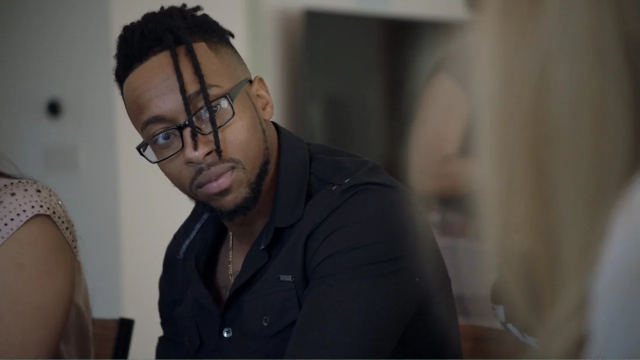 Mary J. Blige's My Life (2021) movie still: medium — A well-lit indoor space with light-colored walls and blurred foreground elements. A man in a…