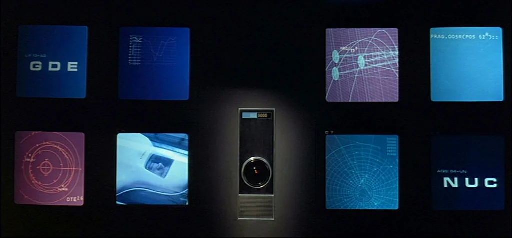 2001: A Space Odyssey (1968) movie still: establishing — A dark console wall features eight small square monitors displaying technical graphics and…