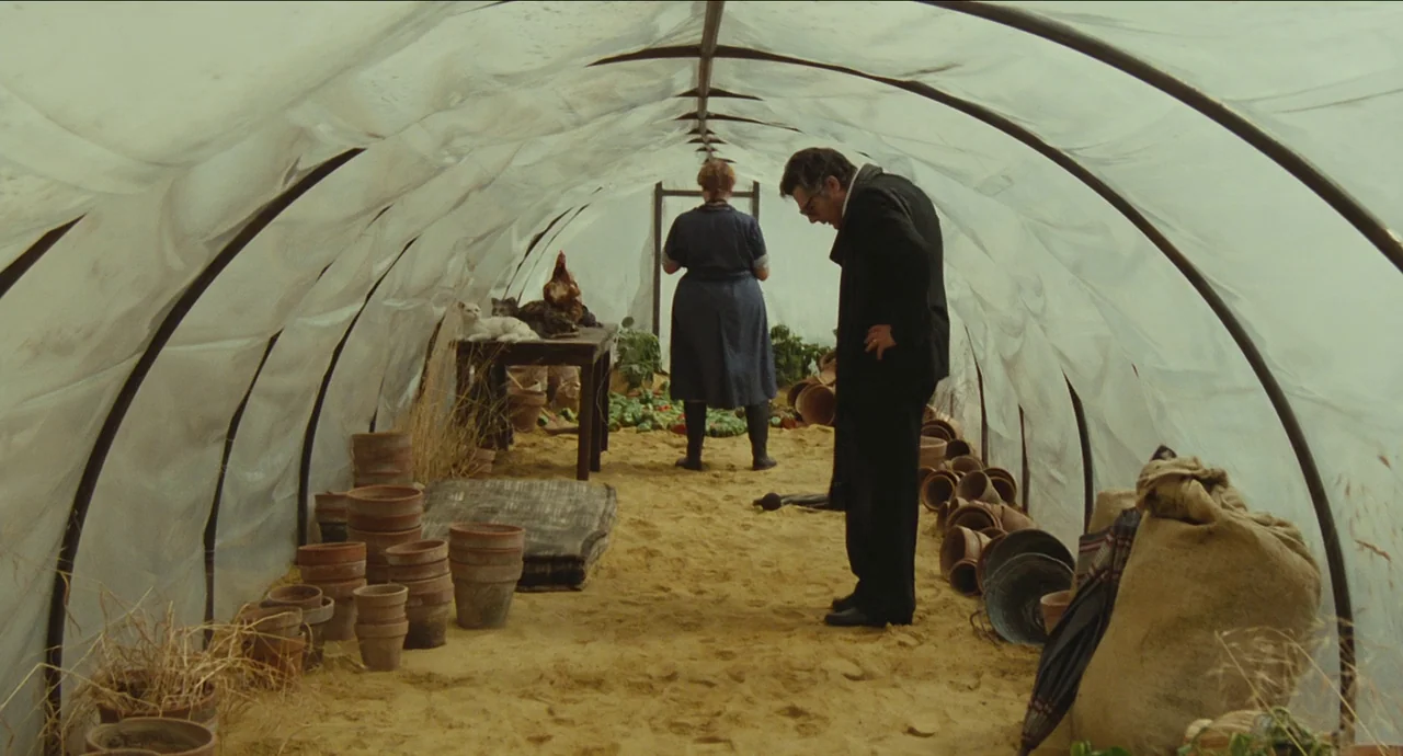 City of Women (1980) movie still: fullbody — A plastic-walled hoop house with a sandy floor filled with terracotta plant pots. A man and a woman…