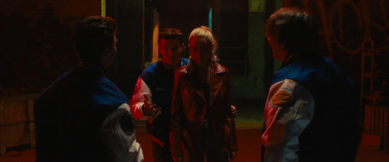 Freaky (2020) movie still: medium — A dimly lit interior with a dark, enclosed atmosphere and textured, shadowy walls. Four teenagers are positioned…