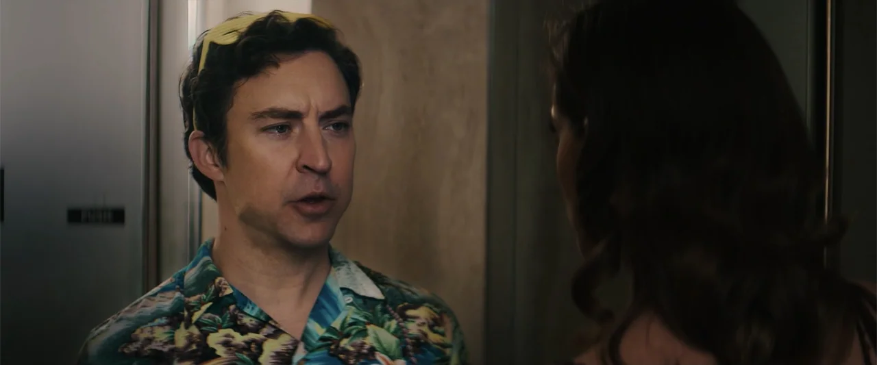 M3GAN 2.0 (2025) movie still: medium — A man stands inside a modern interior elevator with plain panel walls. He is speaking while looking slightly…