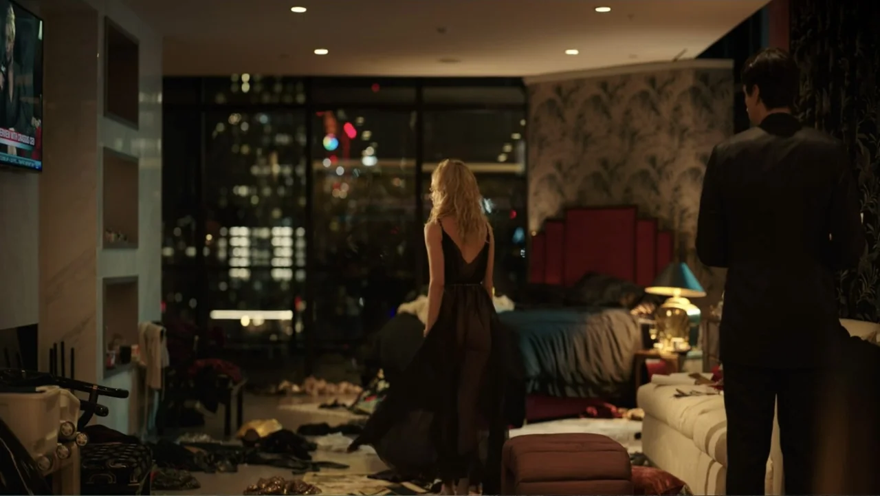 Megalopolis (2024) movie still: fullbody — A dark hotel suite at night contains cluttered clothing items scattered on the floor. A woman in a dark…