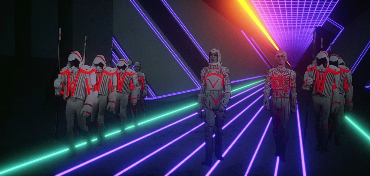 Tron (1982) movie still: wide — A dark digital expanse features receding lines of purple neon and a grid. Multiple figures in white suits with…
