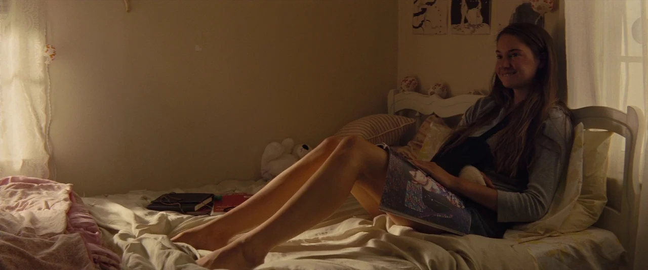 The Spectacular Now (2013) movie still: medium — A teenage girl sits on her bed in a sunlit room filled with personal mementos. She holds an open…