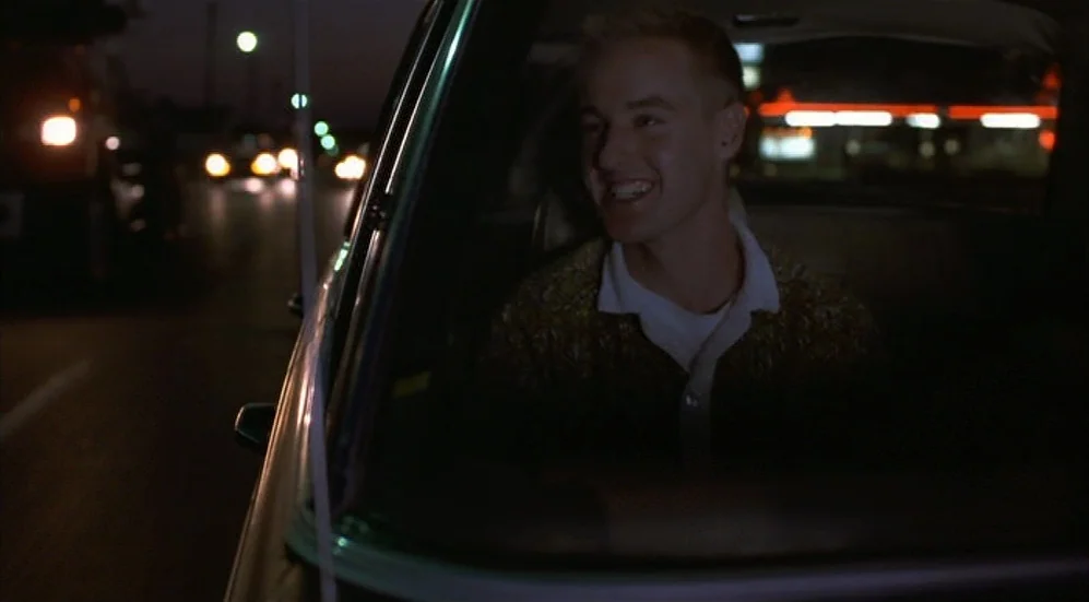 Bottle Rocket (1996) movie still: medium — A dark night street viewed from the passenger side of a moving car interior. A young man sits in the…