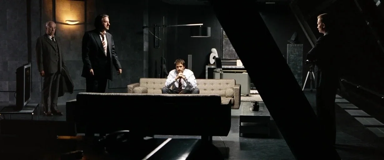 The International (2009) movie still: wide — A large dark penthouse apartment features dark walls and a minimalist furniture layout. Four men stand…
