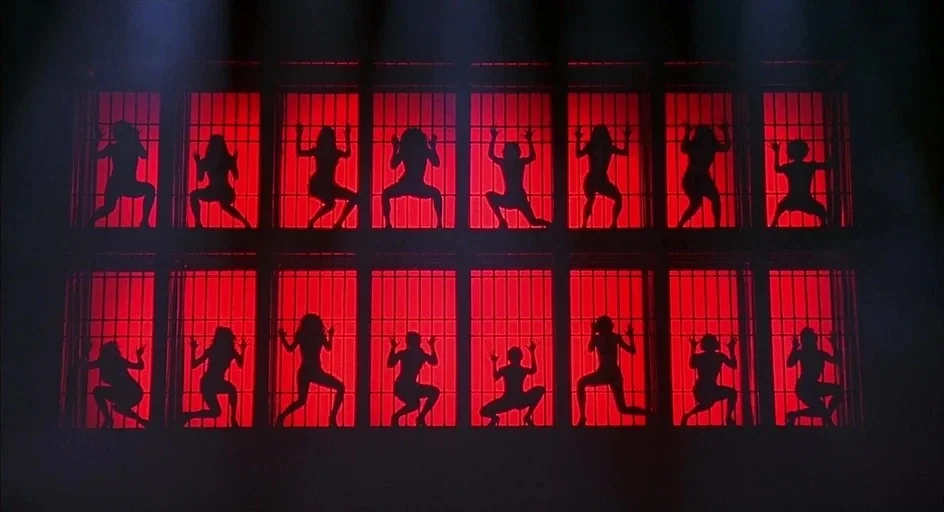 Chicago (2002) movie still: wide — A dark performance stage features sixteen vertical cages glowing with intense red light. Women in tight…