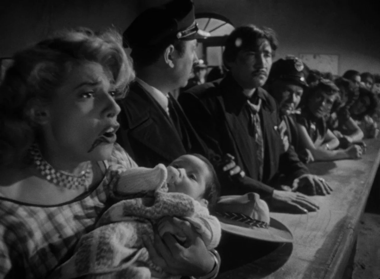 Victims of Sin (1951) movie still: medium — A line of people stands before a long counter at a dark border checkpoint. A woman with a baby in her…
