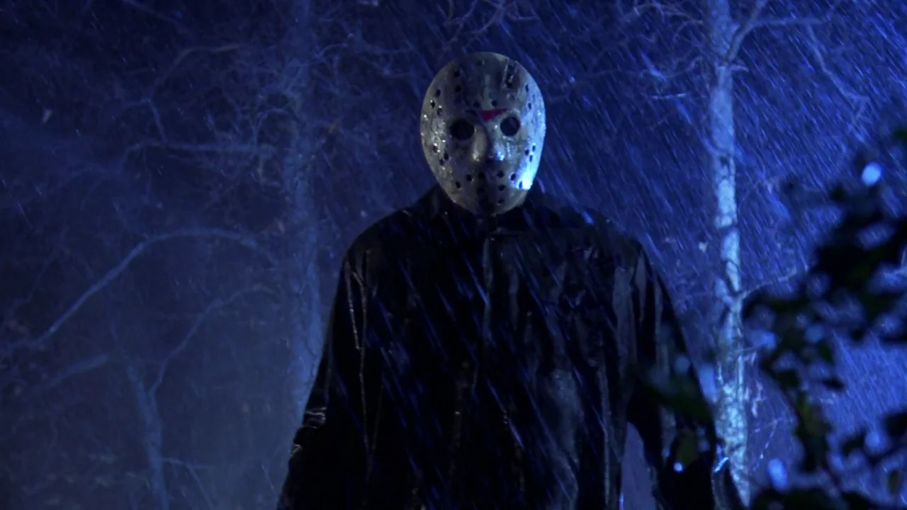 Friday the 13th: A New Beginning (1985) movie still: medium — A dark, rain-drenched outdoor area with trees silhouetted against a deep blue night…