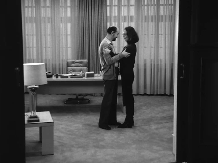 From the Life of the Marionettes (1980) movie still: fullbody — A minimalist professional space features a large desk with sheer curtains covering…