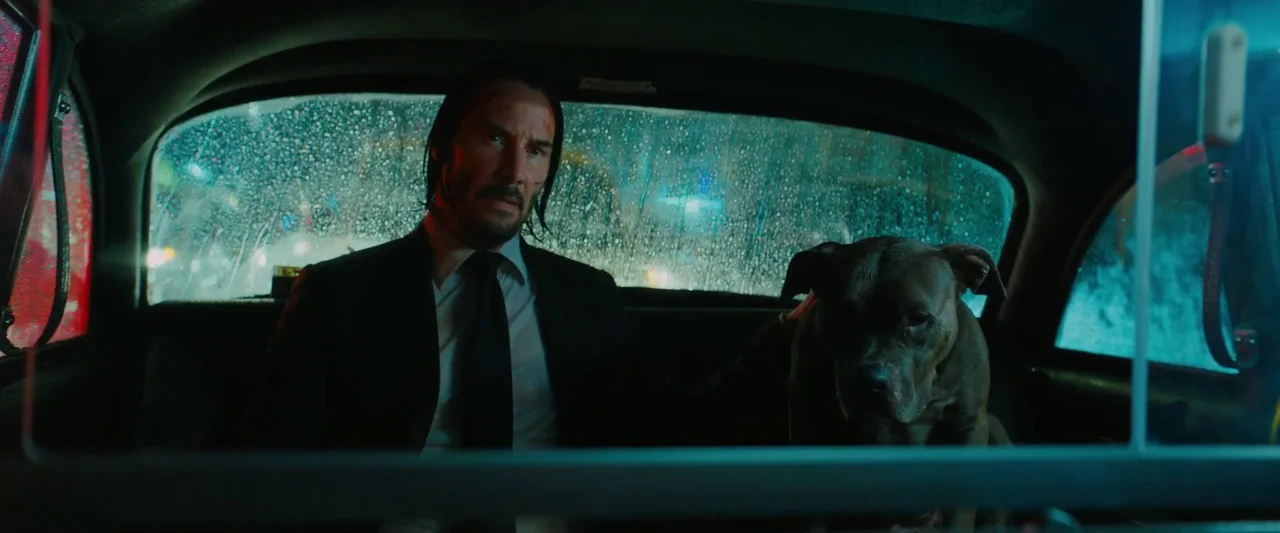 John Wick: Chapter 3 – Parabellum (2019) movie still: medium — The interior of a moving car is dark and cold at night with rain. A man in a dark…