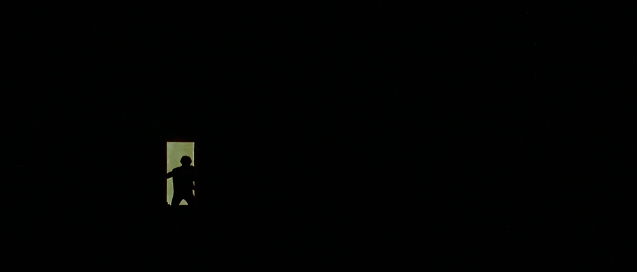 The Bird With The Crystal Plumage (1970) movie still: wide — A dark, empty space frames a single, brightly lit rectangular doorway in the distance.…