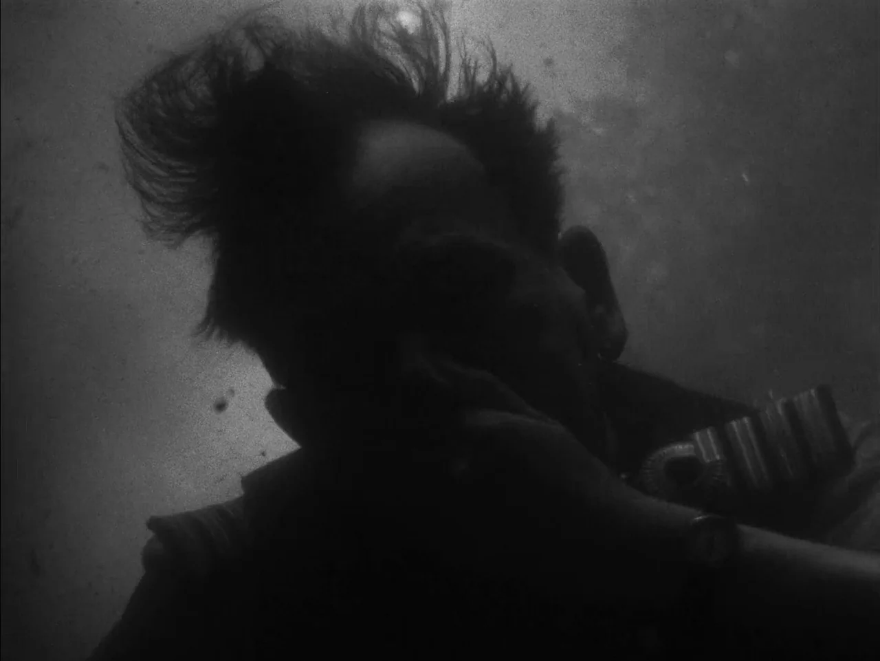 In Which We Serve (1942) movie still: closeup — A dark, cramped interior space with metallic textures and particles drifting in the air. A man in a…