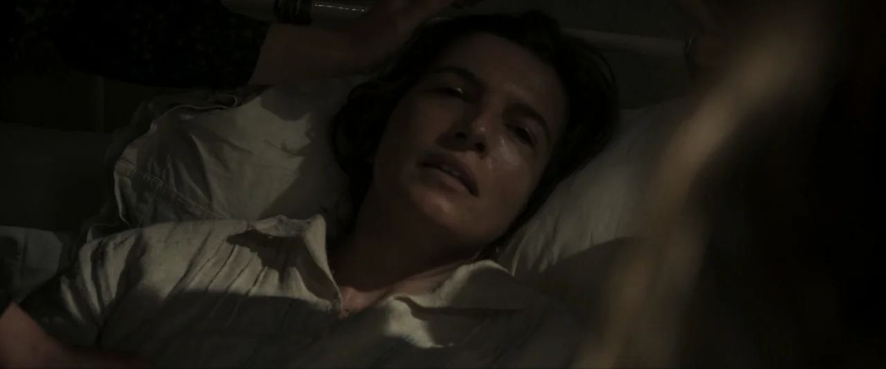 Fatima (2020) movie still: closeup — A dark bedroom interior with a woman lying on a white pillow. The woman rests her head on the bedding while…