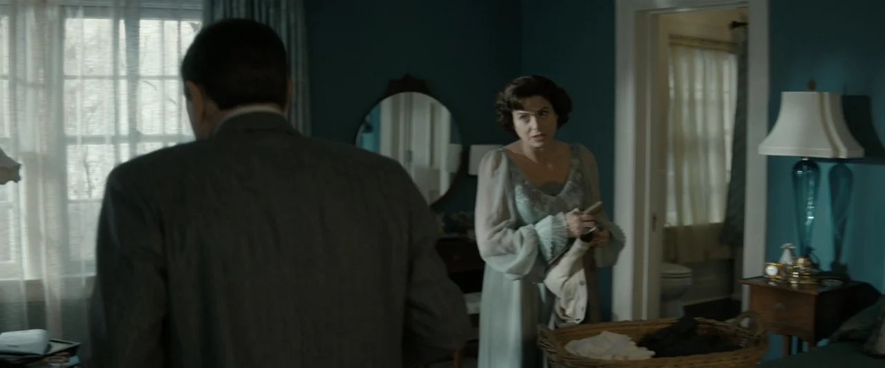 The Alto Knights (2025) movie still: medium — A 1940s style bedroom features dark teal walls, a vanity mirror, and laundry basket. A woman stands…