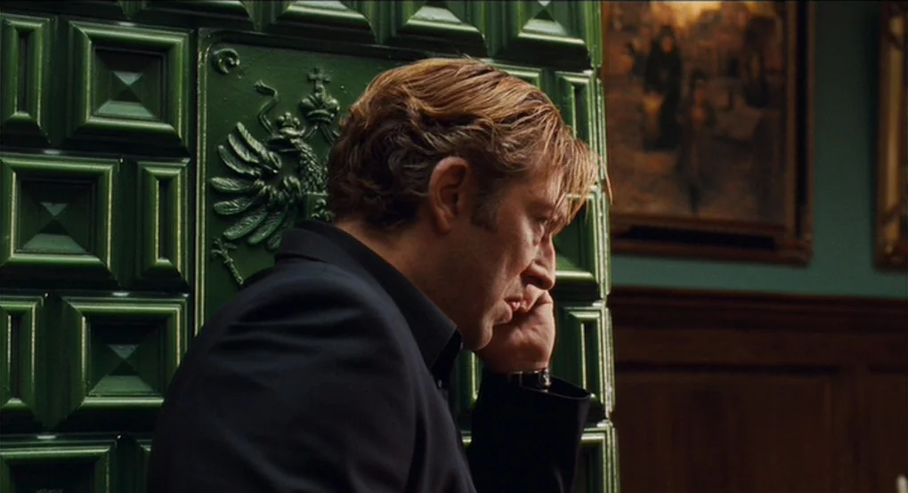 Eastern Promises (2007) movie still: medium — A man stands indoors next to a decorative green ceramic heater with imperial crests. The man is…