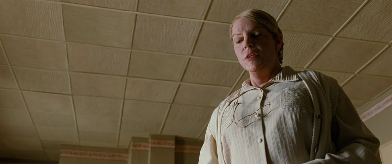Cloud Atlas (2012) movie still: medium — A woman stands in a room with a drop-tile ceiling and pale beige walls. She looks downward while wearing a…