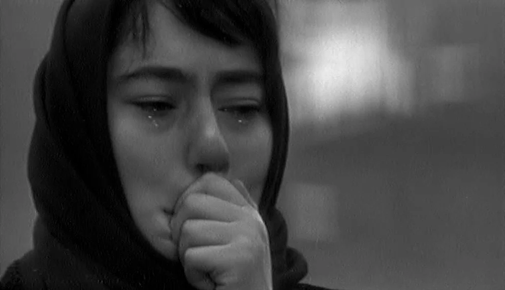 The Plea (1968) movie still: closeup — An outdoor setting features a woman with a headscarf in monochrome tones. She holds her hand to her mouth…