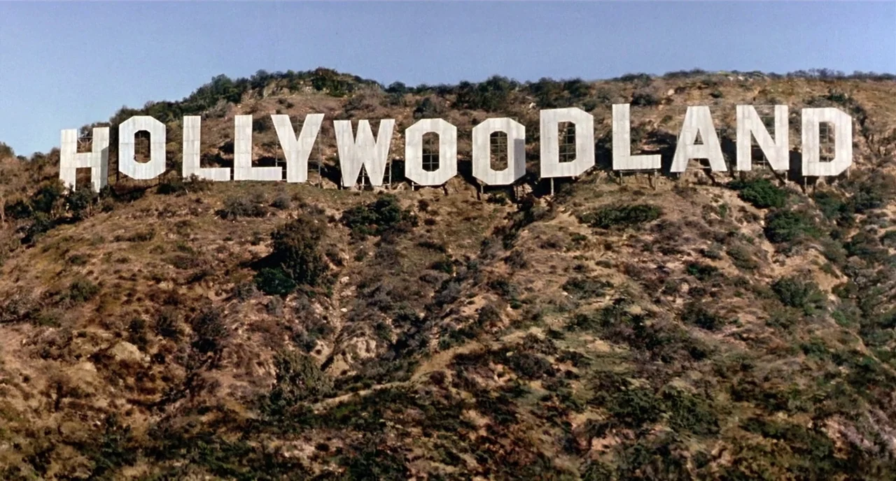 Chaplin (1992) movie still: establishing — The Hollywoodland sign rests on the face of a dry, brush-covered mountain. The large white letters are…